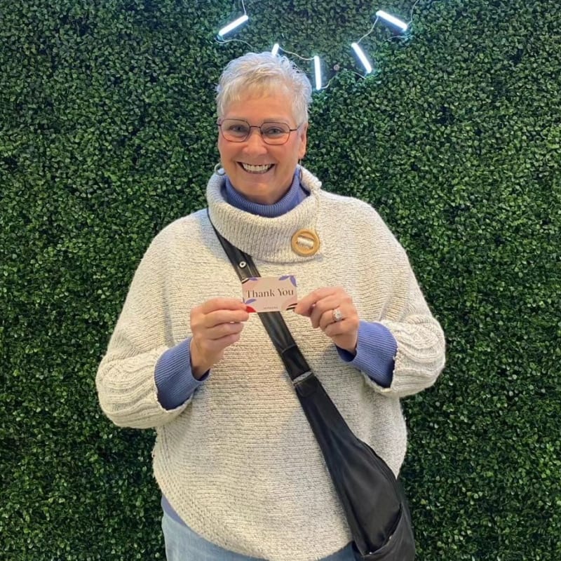 A patient at Dr. Lesley Williams stands with a patient at South Surrey Smiles. smiles and holds a thank you card.