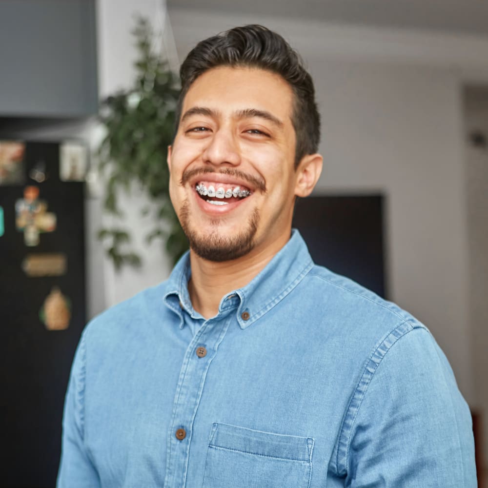 A man in a denim shirt smiles showing his braces.