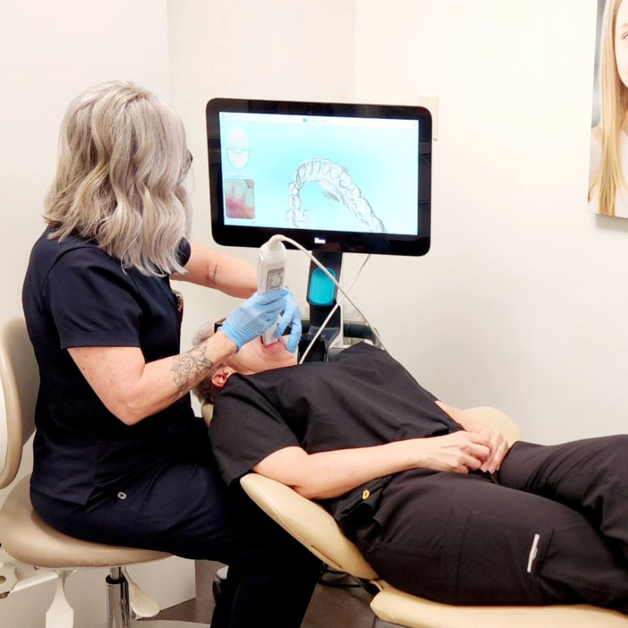 A team member at Dr. Lesley Williams stands with a patient at South Surrey Smiles uses a 3D scanner on a patient's mouth.