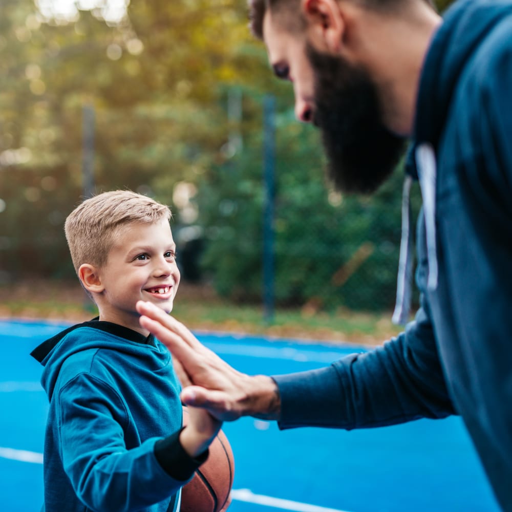A kid high-fiving his dad on an outdoor basketball court.