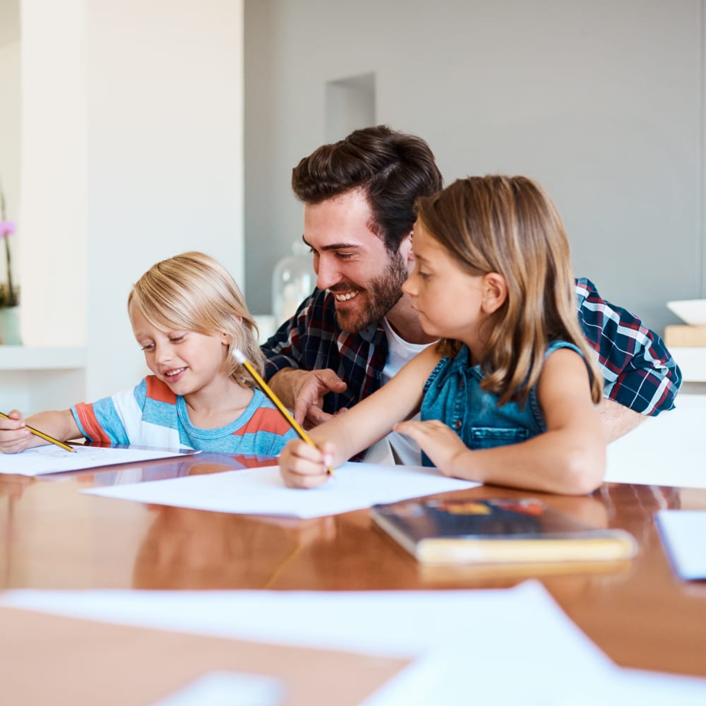 A father an his two children sitting at the table and writing on paper.
