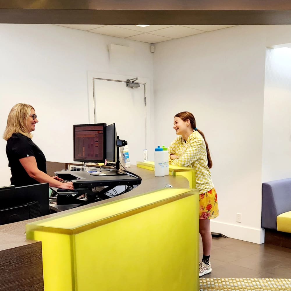 A patient stands at the South Surrey Smiles front desk talking to the receptionist.